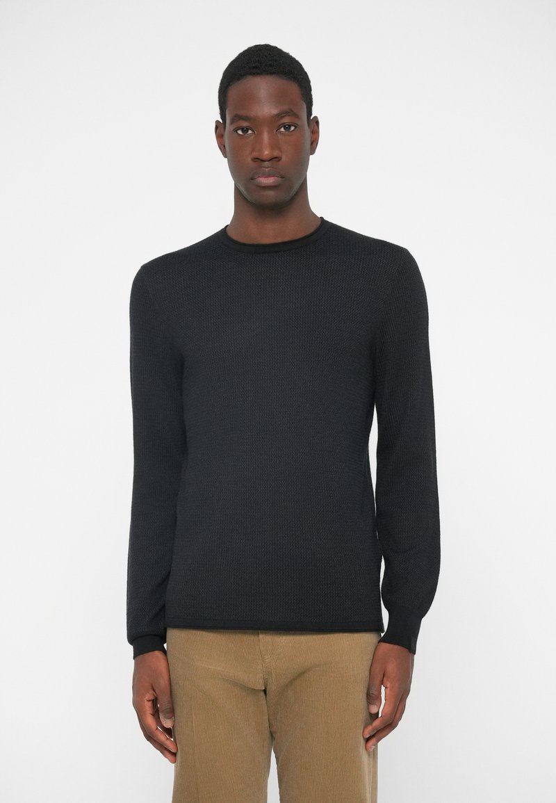Black long-sleeve sweater with a textured pattern and round neckline, paired with beige corduroy pants. Minimalist design, fitted silhouette.