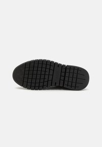 Black rubber shoe sole featuring a textured grip pattern with horizontal and vertical lines, rounded toe, and embossed branding.