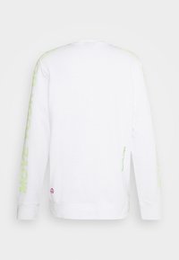 Pitkähihaisen valkoisen t-paidan, joka on valmistettu puuvillasta, hihoissa on vihreää tekstiä "MOVE YOUR" ja helmoissa pieni vaaleanpunainen rauhansymboli.