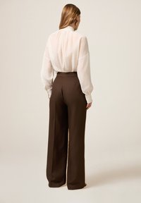 Lange mouwen, lichtbeige blouse met een hoge hals, gecombineerd met high-waisted, brede bruine broeken. Glad, vloeiend textuur van de stof.