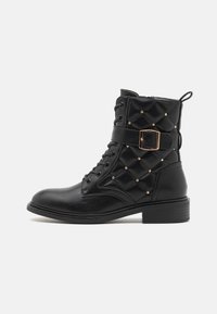 Bottines noires à lacets avec un dessus matelassé, des rivets dorés et des details de boucle. Présente un petit talon épais et une semelle robuste.