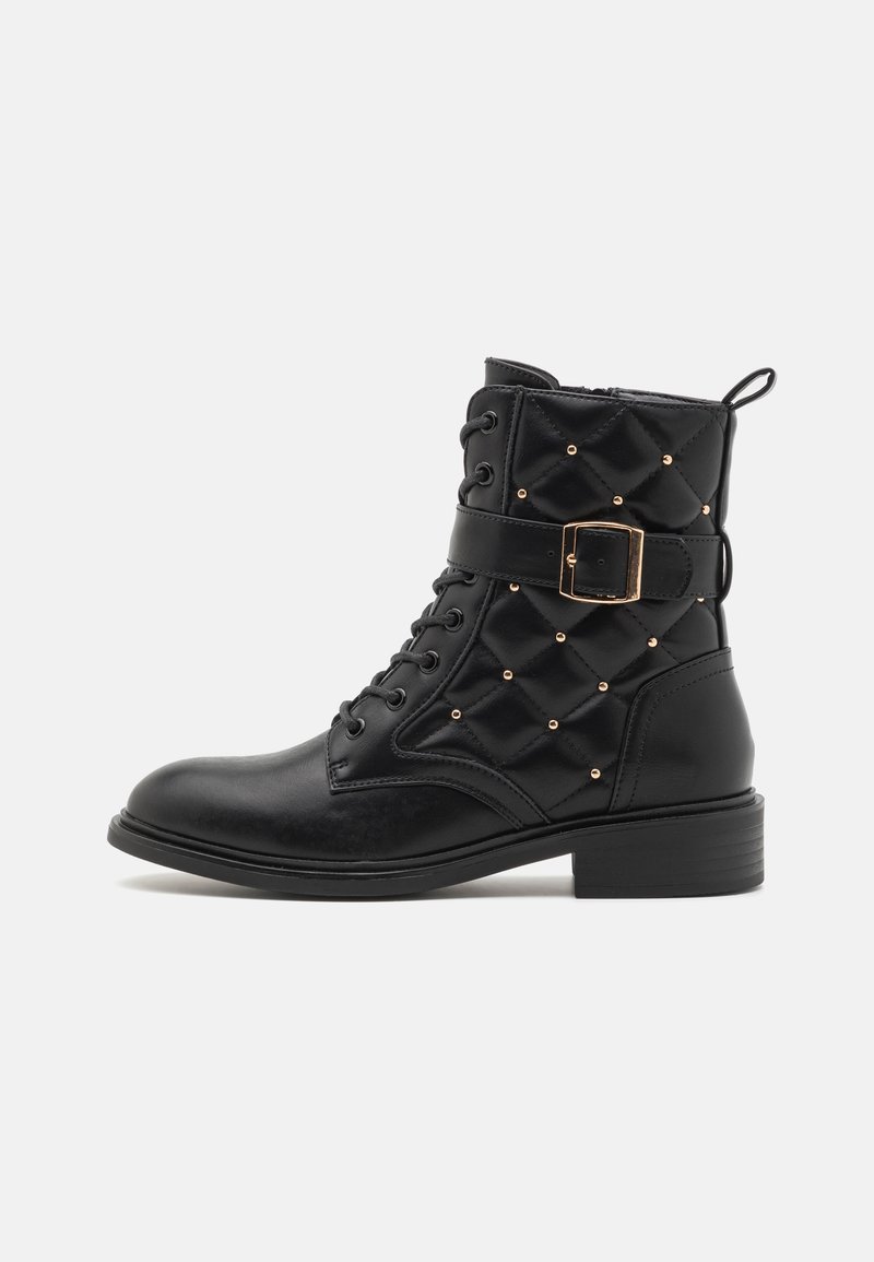 Bottines noires à lacets avec un dessus matelassé, des rivets dorés et des details de boucle. Présente un petit talon épais et une semelle robuste.