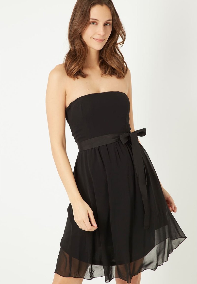Vestido negro sin mangas con un cuerpo ajustado, falda de chifón fluida y detalle de cinturón atado en la cintura. Tejido suave, con dobladillo a la altura de la rodilla.