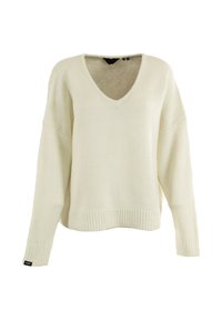 Maglione a V di colore crema con orlo e polsini a coste, maniche lunghe e una piccola etichetta nera sul polsino sinistro.