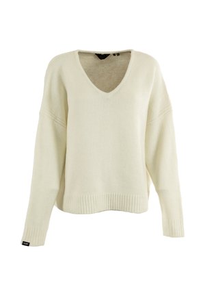 Suéter de punto en color crema con cuello en V, con dobladillos y puños acanalados, mangas largas y una pequeña etiqueta negra en el puño izquierdo.
