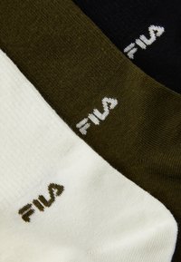 Three pairs of socks in black, olive green, and white. Each pair features a logo. The material appears soft with a smooth texture.