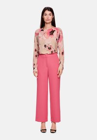 Blumenbluse mit langen Ärmeln in Beige und Rosa, kombiniert mit hoch taillierten rosa weit geschnittenen Hosen. Schwarze Sandalen mit offenem Zehenbereich.