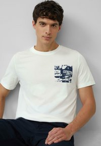 Witte katoenen T-shirt met een blauwe grafische print van een motelsignaal op de linkerkant van de borst. Ronde halslijn en korte mouwen.