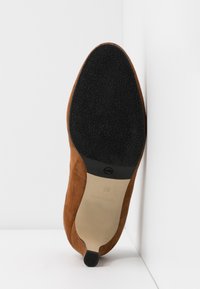 Chaussure pour femme en daim marron vue de la semelle, avec l'avant texturé noir, la partie centrale beige, et un petit talon noir.