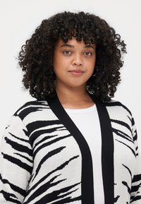 Zebra print cardigan featuring a soft knit texture, black and white color scheme, open front, and contrasting black trim.