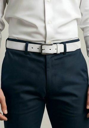 Mann trägt ein weißes Hemd mit Knöpfen, das in dunkelblaue Hose gesteckt ist, mit einem weißen, strukturierten Gürtel und einer silbernen Schnalle mittig in der Taille.
