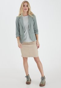 En ljusgrön blazer över en grå och vit randig topp, tillsammans med en beige pennkjol och olivgröna snörade anklarstövlar.