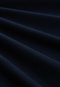 Donkerblauwe stof met een opvallend wafelpatroon, met zachte golvingen en diepte in de weving die de tactiele aantrekkingskracht versterkt.