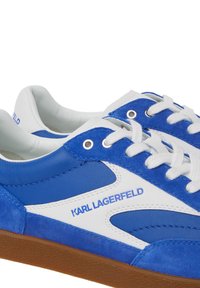 Modri semiš in usnjeni športni čevlji z belimi detajli, okroglo vezanje in teksturiran rjav gumijast podplat. Blagovna znamka v modri barvi na strani.