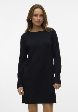 Svart stickad klänning i sweatshirtstil med ett strukturerat sicksackmönster, långa ärmar och en avslappnad passform. Har rund halsringning och sidofickor.