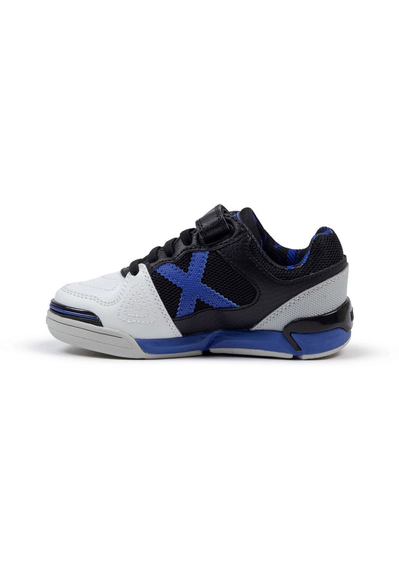 Zapatilla deportiva en blanco y negro con acentos azules, hecha de materiales de malla y cuero, con puntera redondeada, correa de velcro y superficie texturizada en los laterales.