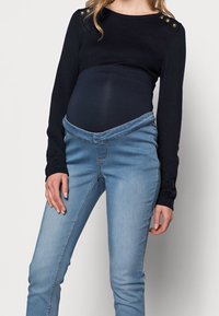 Conjunto de maternidad que incluye una blusa de manga larga en color azul marino con detalles de botones y unos jeans ajustables de color azul claro y elástico.