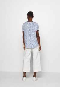 Kurzärmliges, hellblaues Blusenshirt mit einem entspannten Schnitt, kombiniert mit weiten, weißen Hosen und weißen Sneakern. Der Stoff ist weich und leicht.