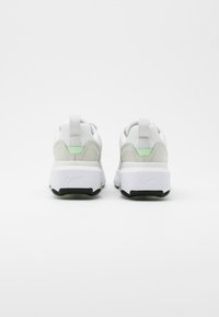 Nike sneakers in white and light grey, featuring a textured upper, padded collar, green accents, and a thick black sole with a white logo.