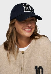 Marineblauwe katoenen baseballcap met een wit en zwart geborduurd "10" logo op de voorkant. Voorzien van een gebogen rand en een verstelbare band.