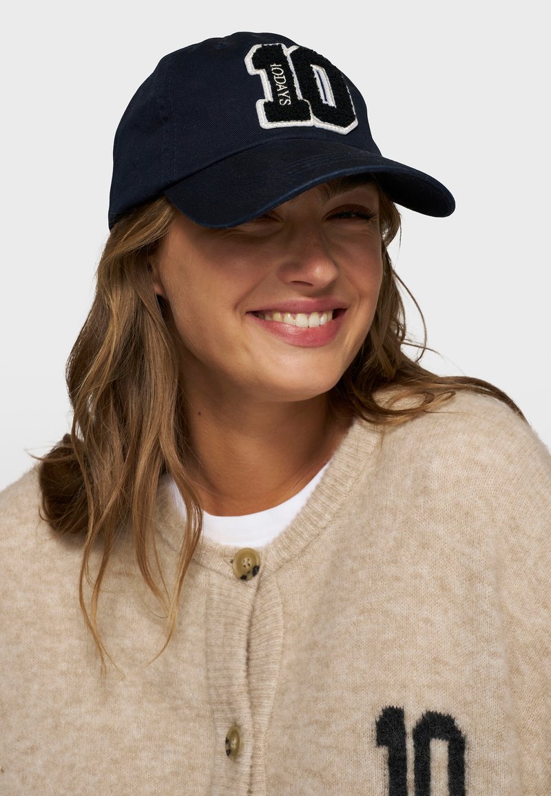Marineblauwe katoenen baseballcap met een wit en zwart geborduurd "10" logo op de voorkant. Voorzien van een gebogen rand en een verstelbare band.