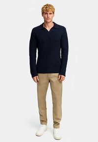 Mørkeblå strikket trøje med V-hals og krave, kombineret med beige bukser og hvide sneakers. Trøjen har et tekstureret stof.