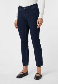 Donkerblauwe skinny jeans met een knoopsluiting, vijf zakken en lichte stikdetails. Gecombineerd met zwarte ballerina's.