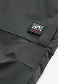 Gros plan sur un tissu foncé avec des coutures cousues et un patch noir carré portant l'inscription "DURATREK" avec un logo de montagne blanc.