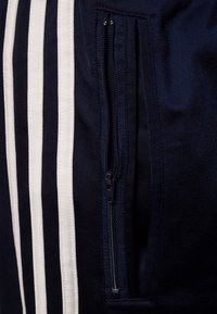 Navy athletic shorts featuring white stripes and a zippered pocket on the side, made of lightweight fabric with a smooth texture.