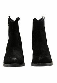 Botines de ante negros con una textura suave, puntera afilada y recortes curvados en los laterales; cuentan con una discreta cremallera lateral y suela de goma plana.