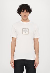 White cotton t-shirt with short sleeves and a round neckline. Features a prominent gray logo on the chest, with a simple design.