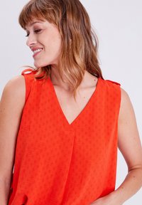 Blusa senza maniche di un vivace arancione con scollatura a V, caratterizzata da un motivo a diamante testurizzato e dettagli con fiocchi sulle spalle.