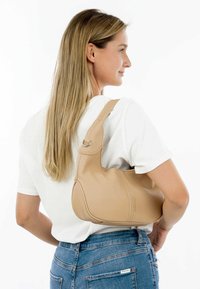 Sac à épaule en cuir beige avec un design courbé, une surface texturée et une seule bandoulière. Présente un accent en anneau sur la bandoulière.