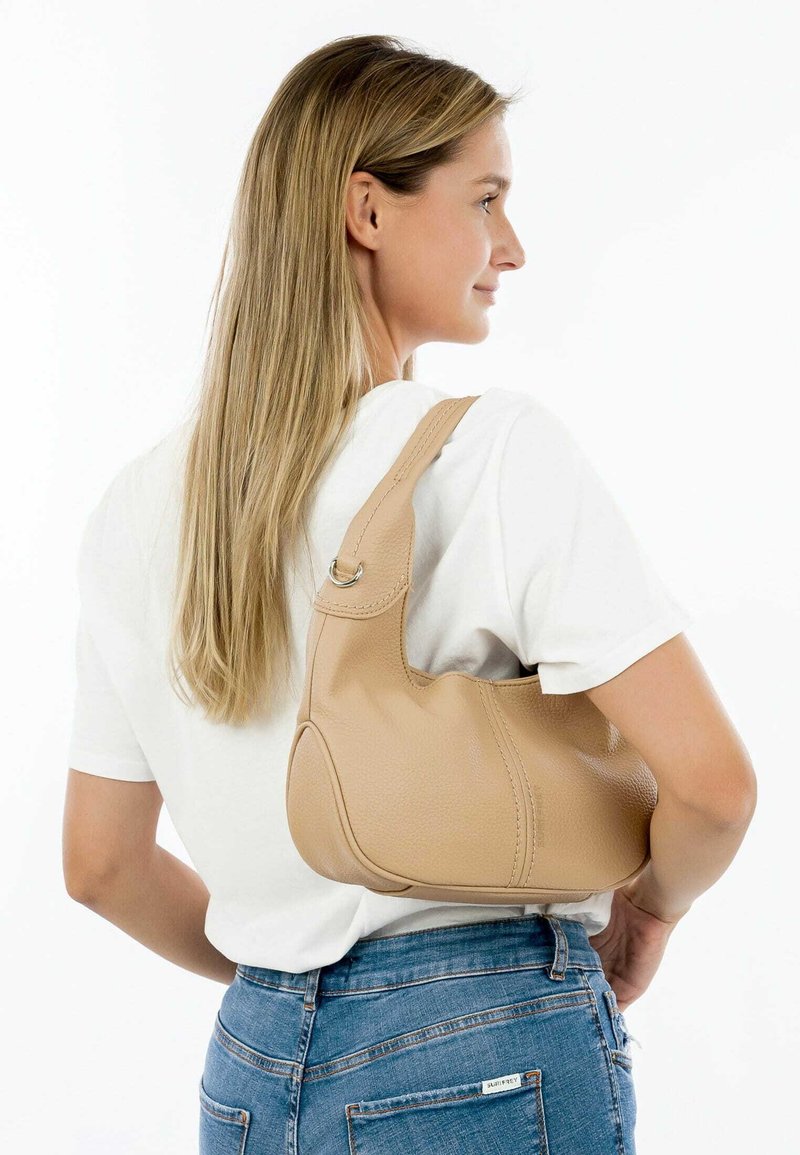 Sac à épaule en cuir beige avec un design courbé, une surface texturée et une seule bandoulière. Présente un accent en anneau sur la bandoulière.