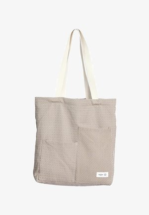 Béžová pruhovaná taška na rameno s dvoma béžovými textilnými popruhmi. Má dve predné vrecká a štítok v pravom dolnom rohu. Vyrobená z organickej bavlny.