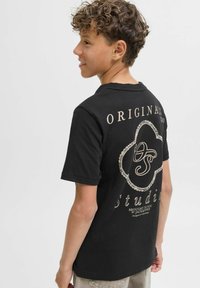 Černé bavlněné tričko s kulatým grafickým designem na zádech a textem "ORIGINAL STUDIO" a ozdobnými detaily, krátké rukávy.