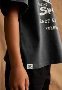 Mørkegrå bomulds T-shirt med et hvidt grafisk print og et vævet label i kanten. Kortærmet og med en afslappet pasform.
