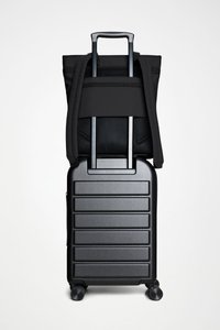 Czarny twardy walizka z prążkowanym wzorem, zintegrowaną chowaną rączką i czarnym plecakiem z tkaniny przymocowanym na górze. Cztery gładko toczące się kółka.