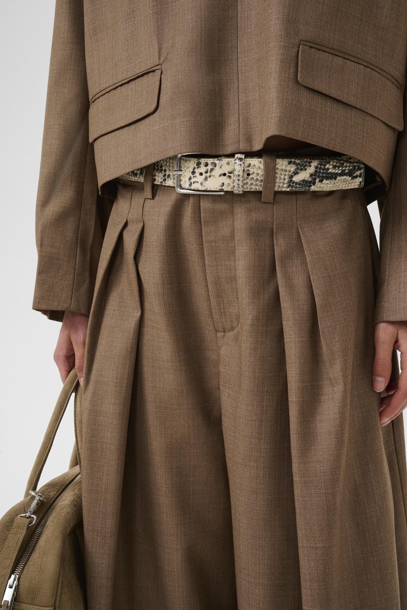 Costume marron sur mesure avec pantalon large plissé, veste courte, ceinture en peau de serpent beige et noire, et sac à main beige texturé assorti.