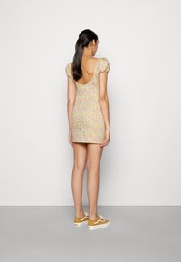 Vestido com estampado floral em cores pastéis, com mangas bufantes e costas em decote baixo. Usado com ténis amarelos e um tecido de textura suave.