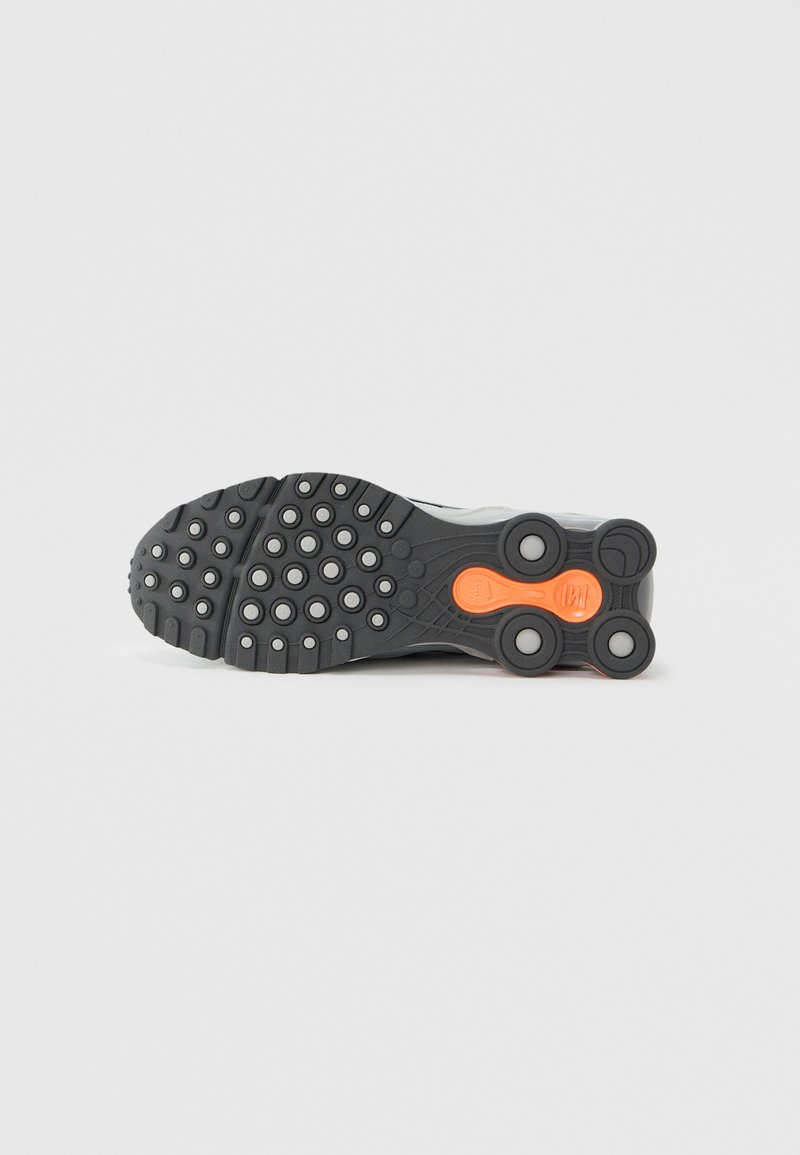Shoe sole with black rubber, circular tread pattern, flexible design, and orange detail. Features pronounced traction and cushioning elements.