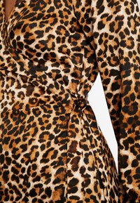 Vestido de estampado de leopardo en tejido ligero, con manchas marrones y negras sobre un fondo beige, con un detalle atado en la cintura y diseño envolvente.