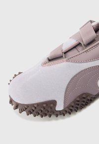 Svetlo vijolični športni čevelj z teksturirano zgornjo plastjo, elastičnimi trakovi in gumijastim podplatom s špičkami za boljši oprijem. Odtisnjen s temnejšimi vijoličnimi detajli.