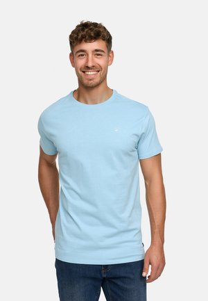 Light blue cotton t-shirt with short sleeves, round neckline, and small logo detailing on the left chest, paired with dark jeans.