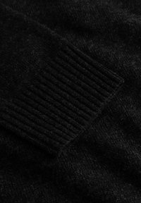 Tricot negru din lână, cu manșete ribbate, textură moale și un aspect ușor melanjat. Vedere în detaliu.