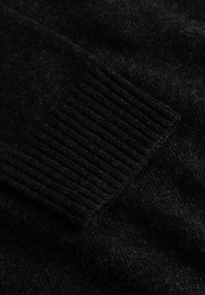 Tissu de pull en tricot noir avec des poignets côtelés, une texture douce et un aspect légèrement chiné. Vue de près sur le détail.