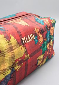 Beauty case rettangolare in tessuto testurizzato con motivo a quadri rosso, giallo e blu. Dettaglio logo dorato sul fianco. Chiusura con zip.