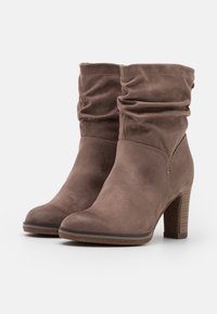 Bottines en daim marron avec un design froissé, bout arrondi et talon marron texturé. Présentent un petit détail près de la cheville.