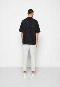 Short-sleeve, dark navy shirt with a textured design, paired with light gray pants and white sneakers. Simple collar and relaxed fit.