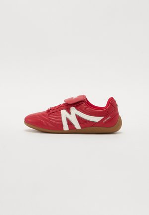 Red athletic shoe with a textured leather upper, white accents, and a strap over the laces. Rubber outsole for traction.